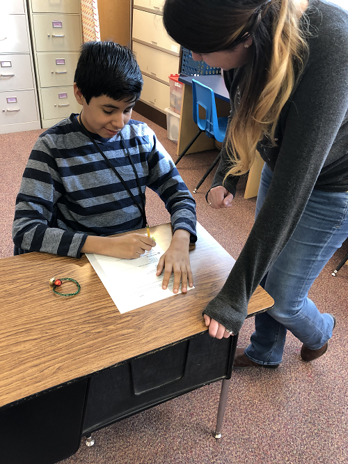 Laura Cuthbertson works with a student sitting at a desk in the classroom.