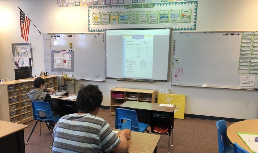 2 students work independently at a desks in a classroom.