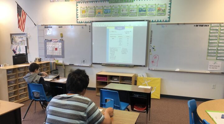 2 students work independently at a desks in a classroom.