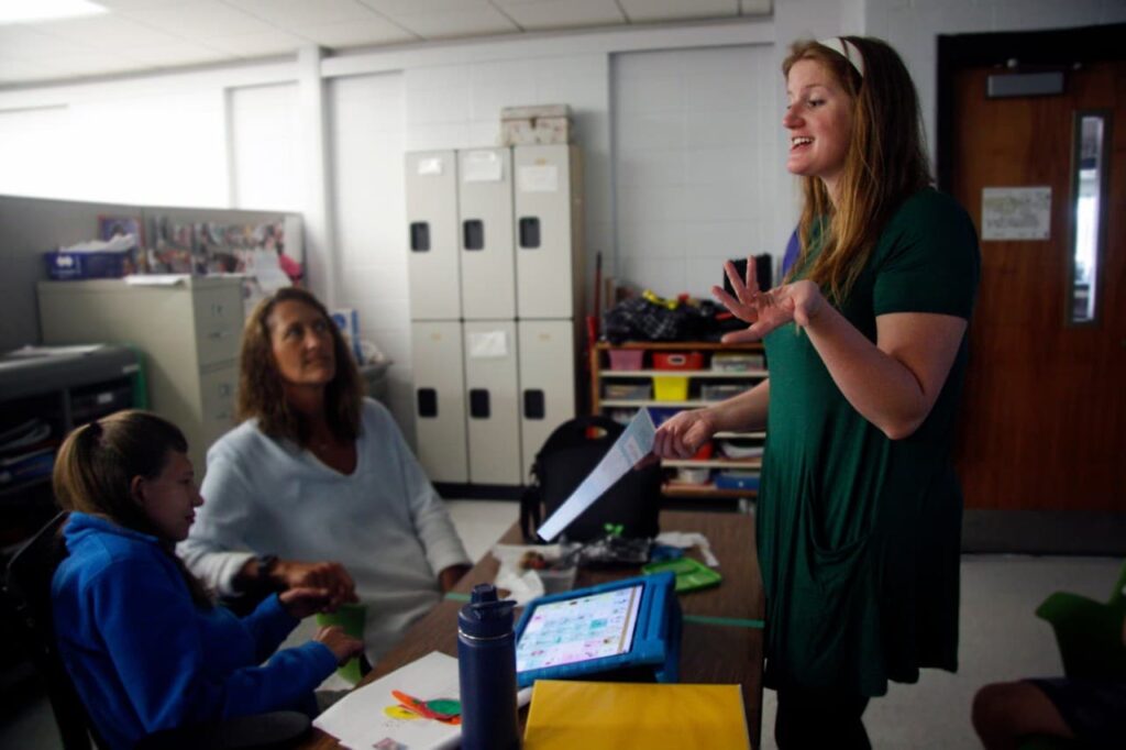Abbey Lynch speaks to two people sitting at desks in a classroom in MacArthur Middle School.