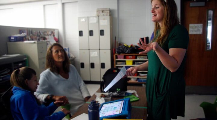 Abbey Lynch speaks to two people sitting at desks in a classroom in MacArthur Middle School.