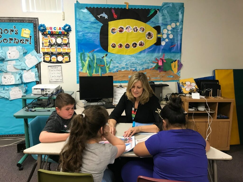 IMG_5926-1-1 Teacher reads at a desk with three children in a classroom