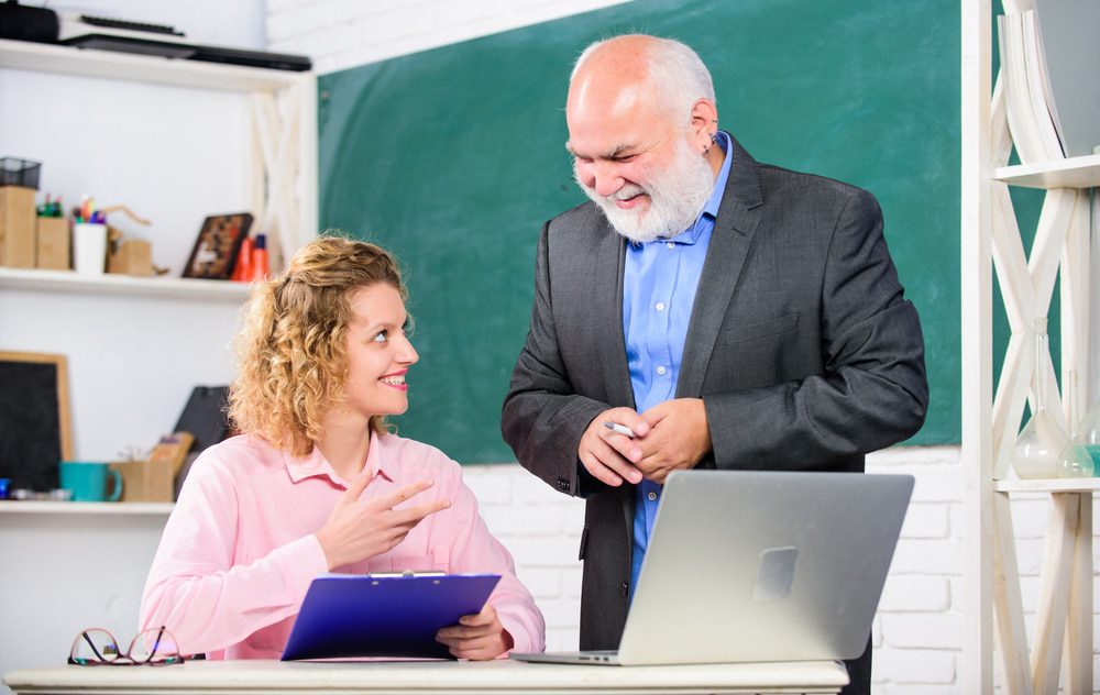 Depositphotos299854884s2019 Building Wings Building Wings Two adults smile at each other while working at a desk