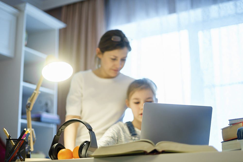 A mother and child look at a laptop together in their home