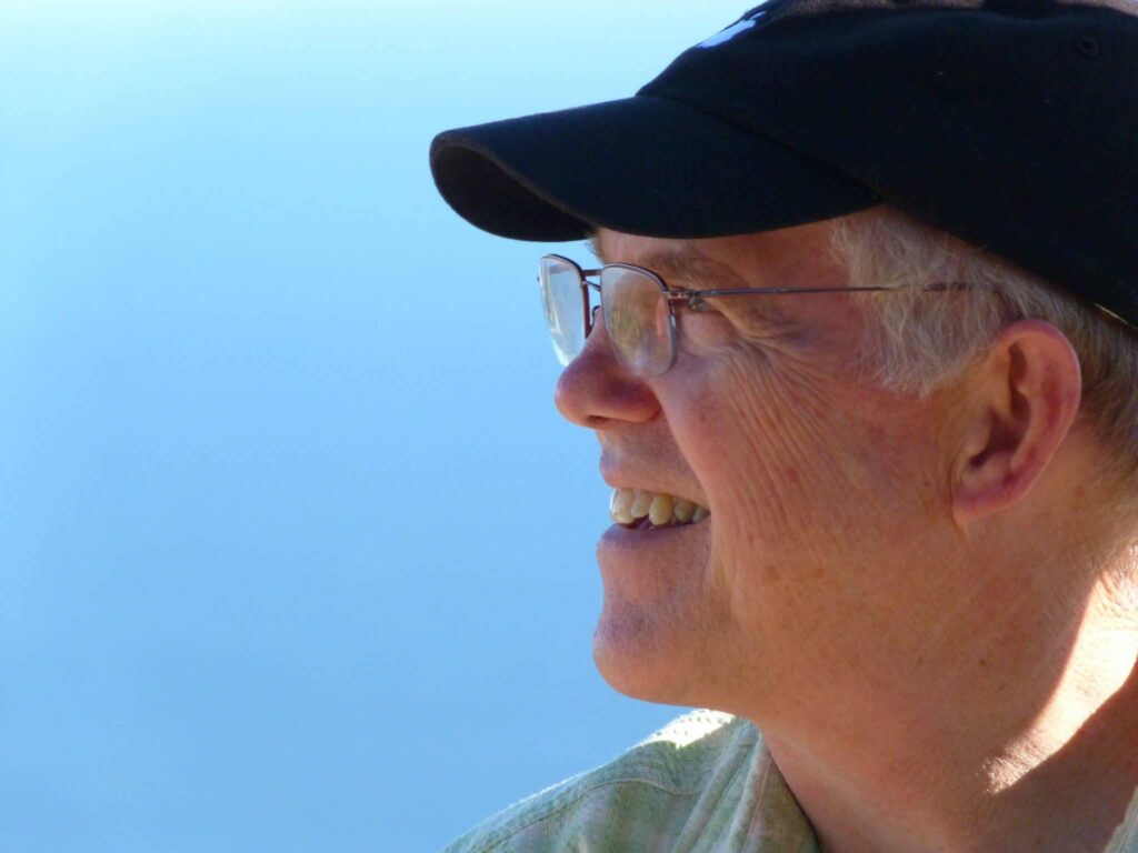 Jerry Stemach smiles while looking off to the side in front of a bright blue sky