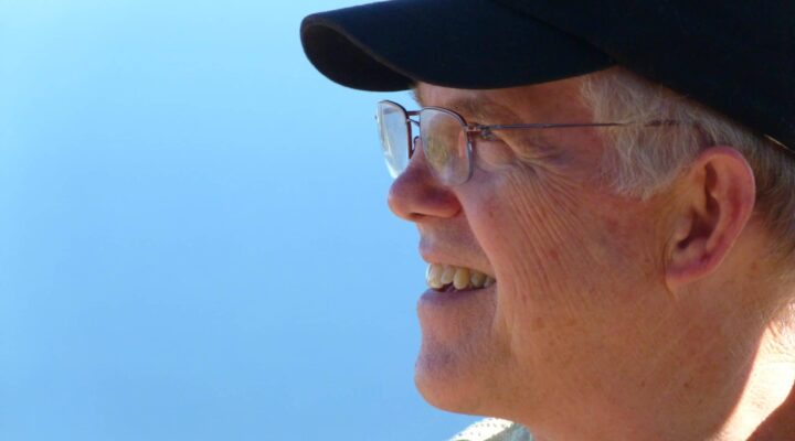 Jerry Stemach smiles while looking off to the side in front of a bright blue sky.