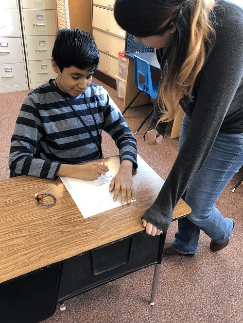 Readtopia transforms the learning experience Building Wings Building Wings A teacher works with a student who is completing a writing activity at a desk in a classroom