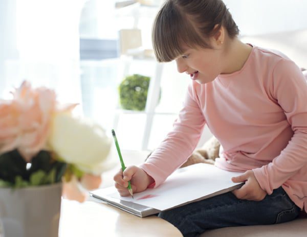 A young girl wearing a pink shirt, writes on a piece of paper.