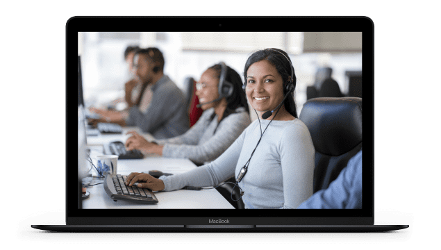 A laptop screen displays a customer service agent smiling at the camera, sitting at a desk while wearing a headset.