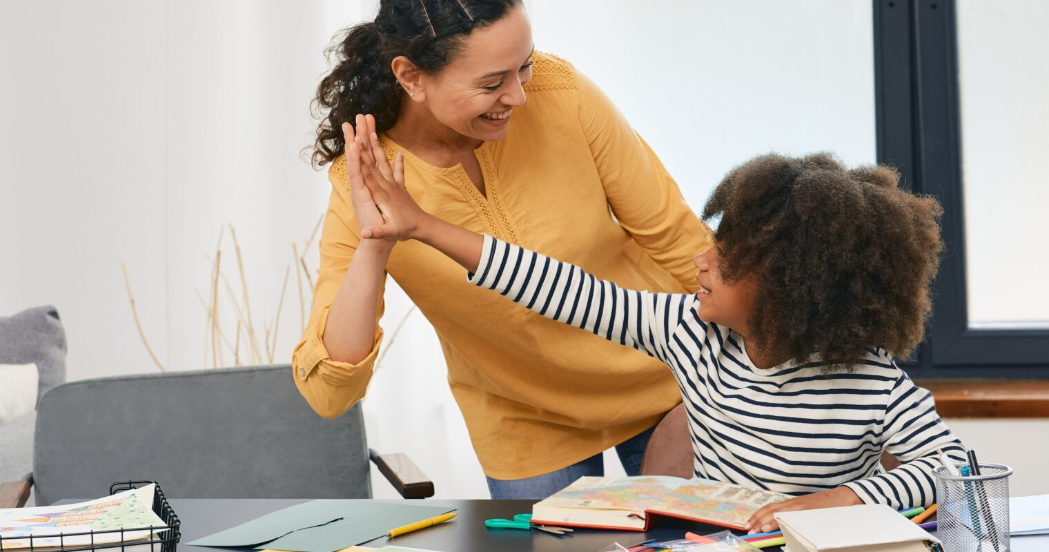 An adult gives a student a high five at a desk.