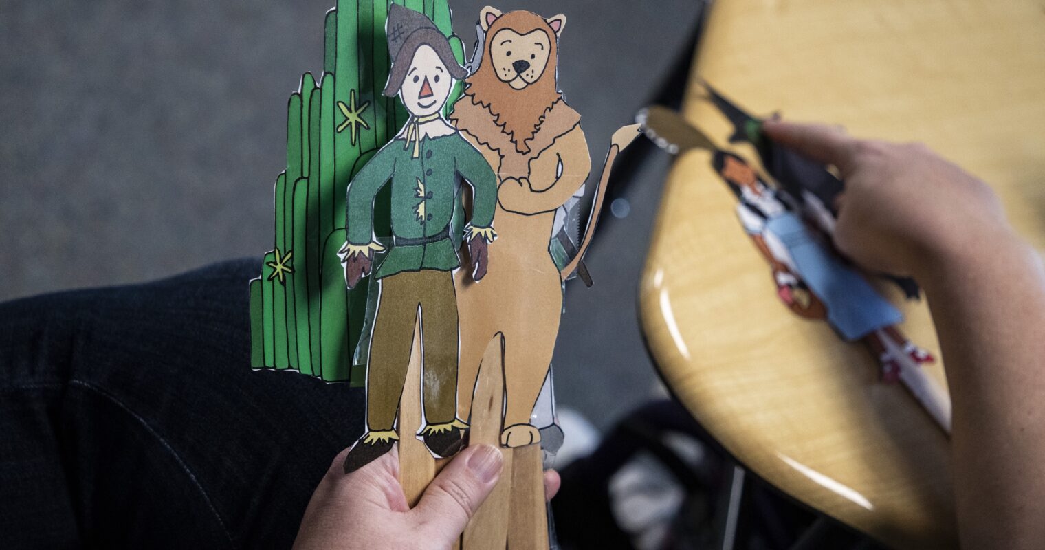 A hand holding paper made stick figures of characters from The Wizard of Oz.