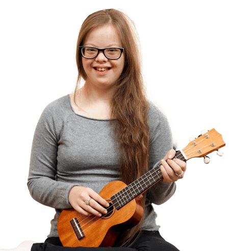 A student in a grey shirt smiles while holding a ukulele