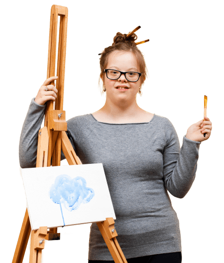 Student in a grey shirt smiles by an easel with artwork on it
