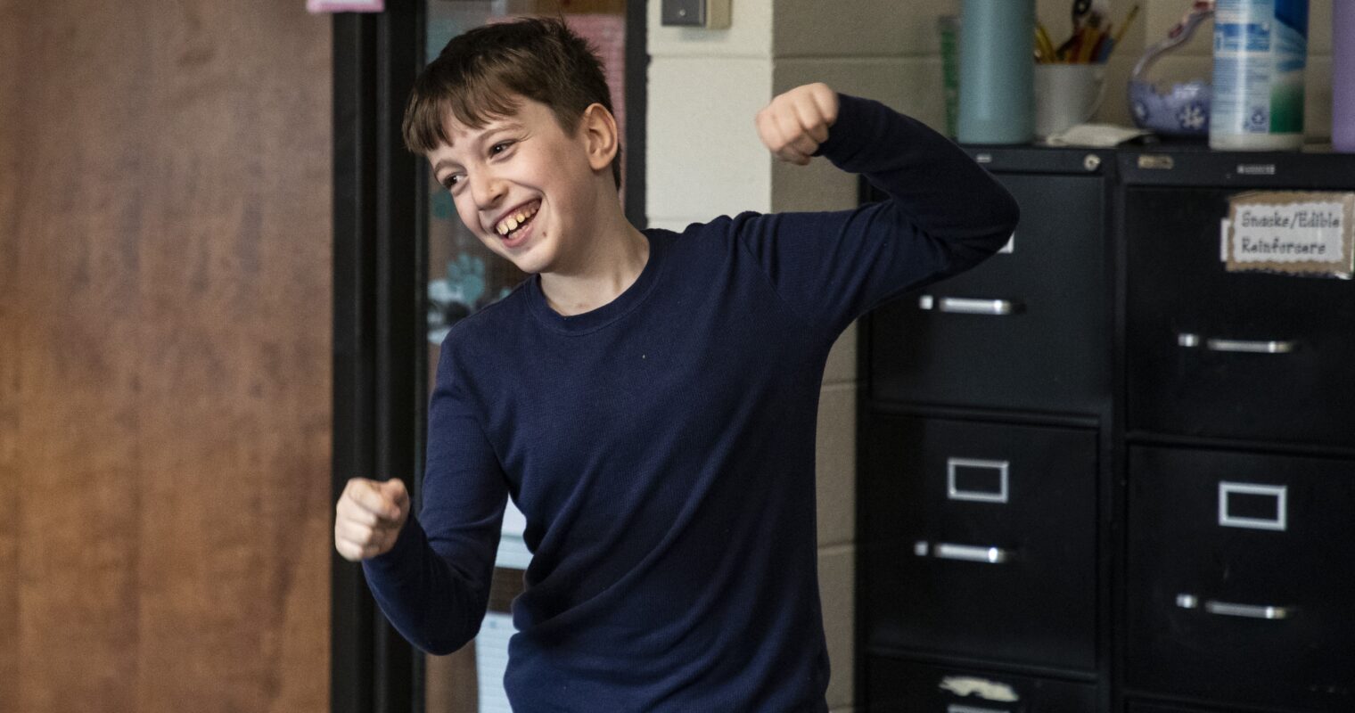 A student in a navy shirt, happily laughing in a classroom.