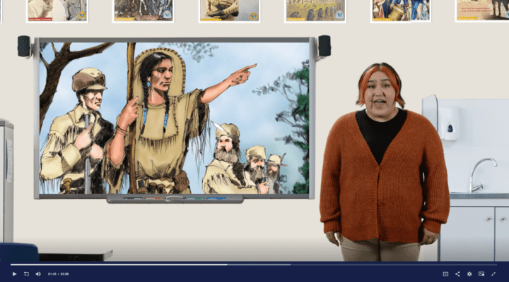 Still video clip of a student next to a smart board with an image of Sacagawea on it.