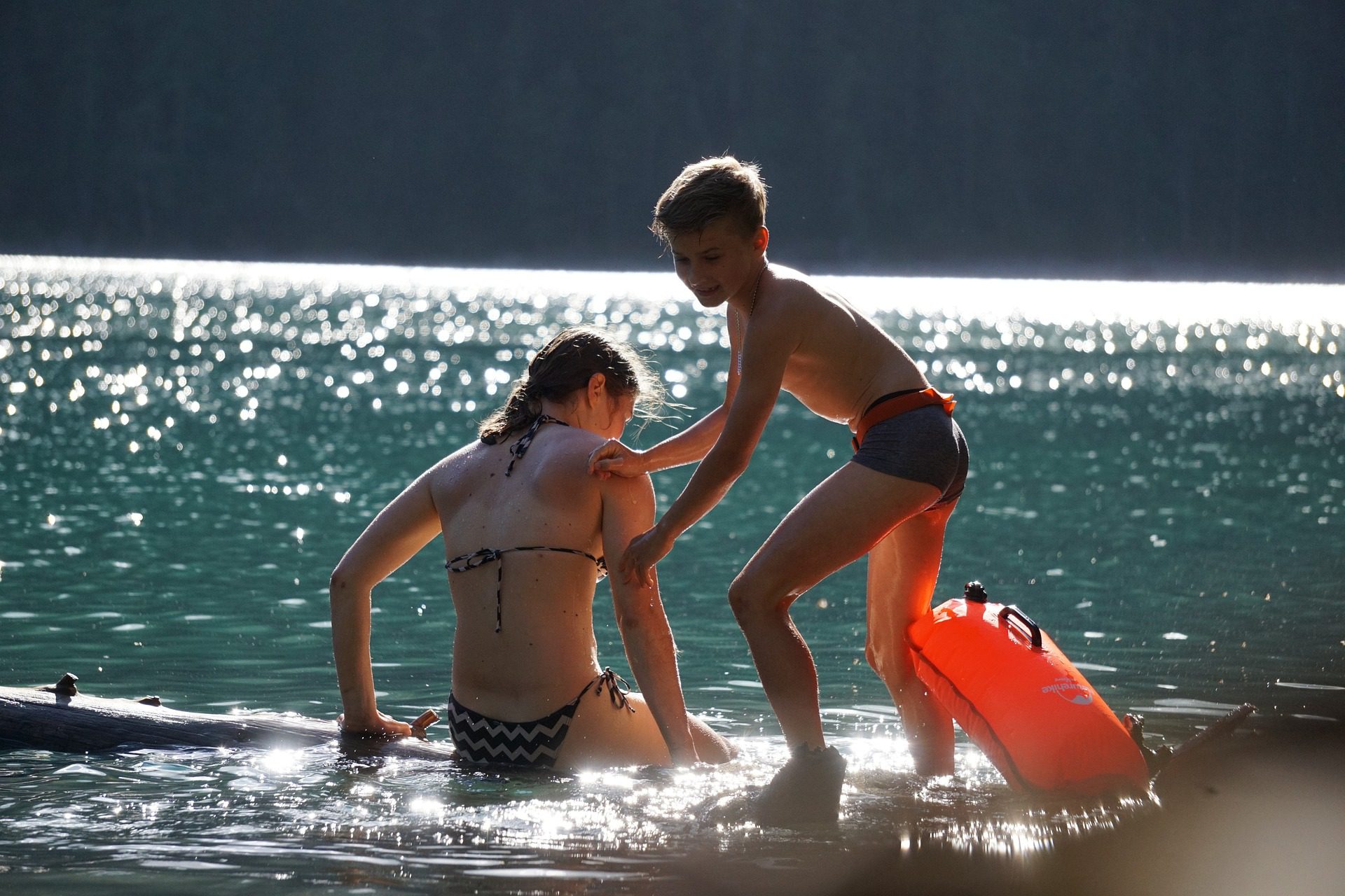 A water scene with a young boy helping a young girl onto a floating raft.