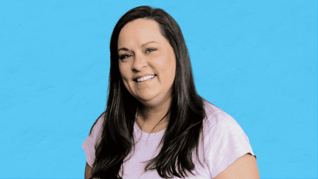 A headshot of a woman, Allison Dennis, with shoulder-length brown hair, wearing a black shirt and necklace, against a blue background.