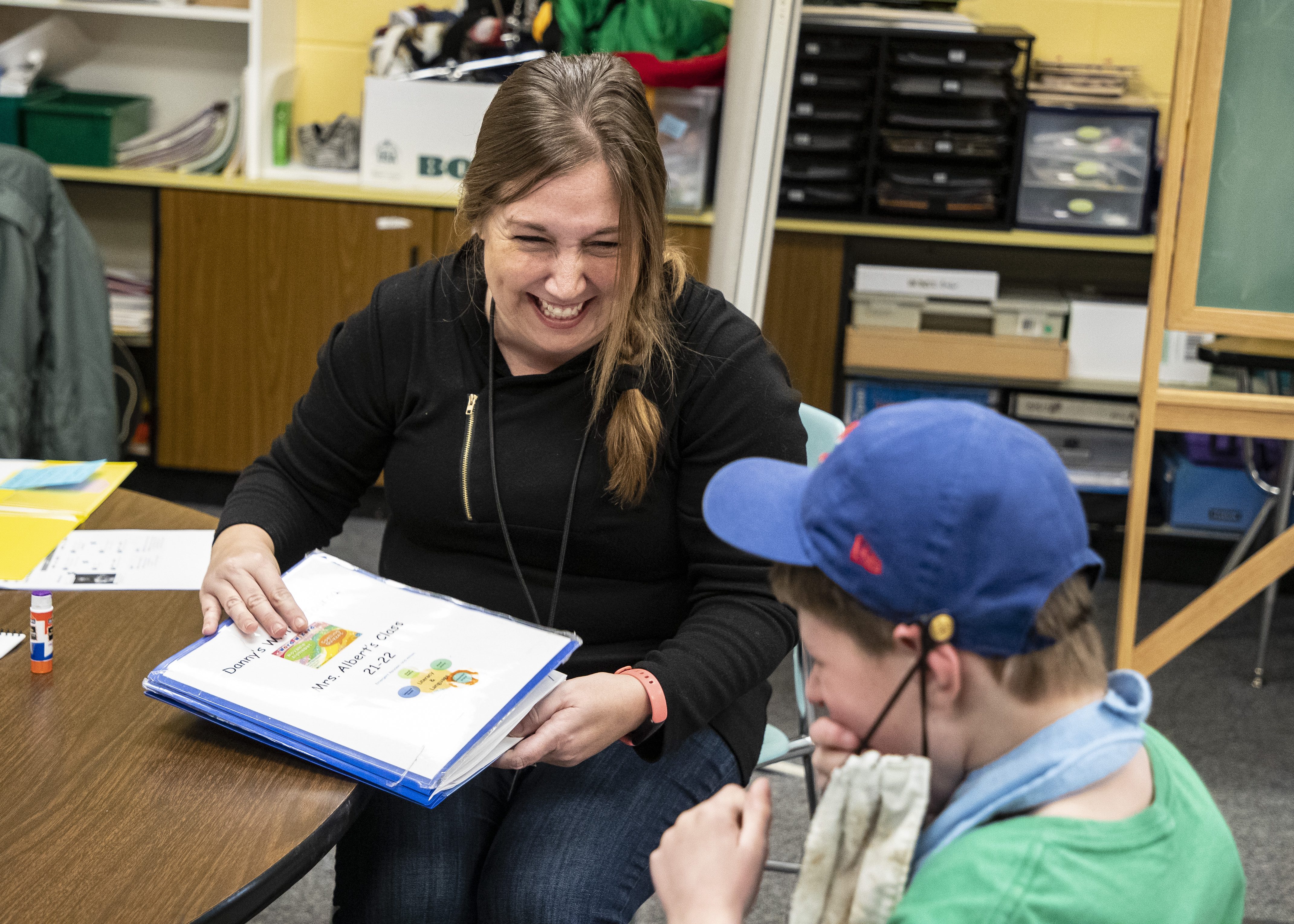 An educator sitting with a young learner while both are looking at literacy learning materials.