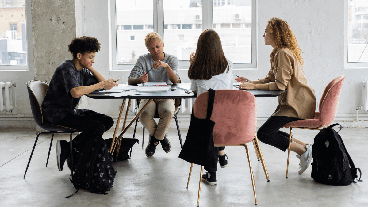 A group of educators seated around a table with a student and with backpacks on the floor.