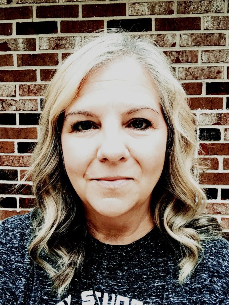 Woman Smiling, blonde hair, dark blue eyes, brick background