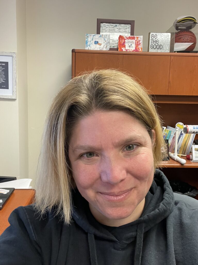 woman smiling, blonde hair, black sweater, in an office.