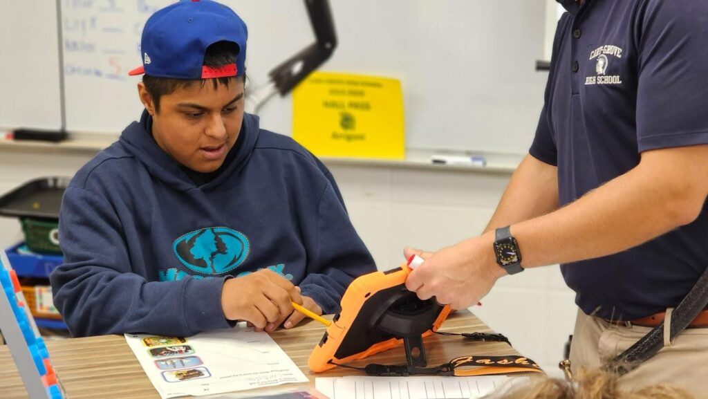 educator provides specially designed instruction to learner in a blue hoodie and blue hat