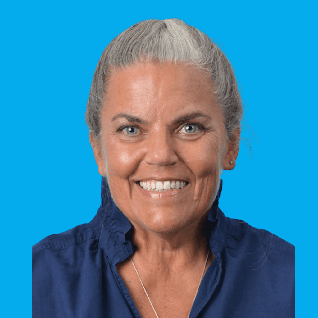 Portrait of a smiling gray-haired woman with hair tied back, wearing a navy blue shirt against a bright blue background.