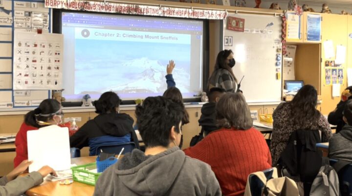 Classroom scene with a masked teacher at the whiteboard and students seated, watching a projection that reads 'Chapter 2: Climbing Mount Sneffels'. Valentine banner overhead.