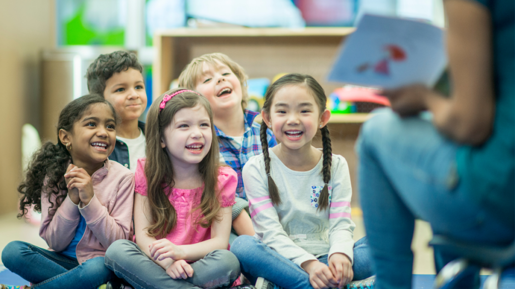 Elementary students smile and engage as their teacher reads a book aloud during shared reading.