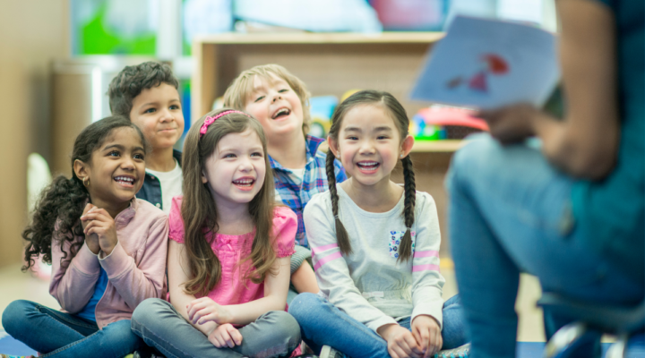 Elementary students smile and engage as their teacher reads a book aloud during shared reading.