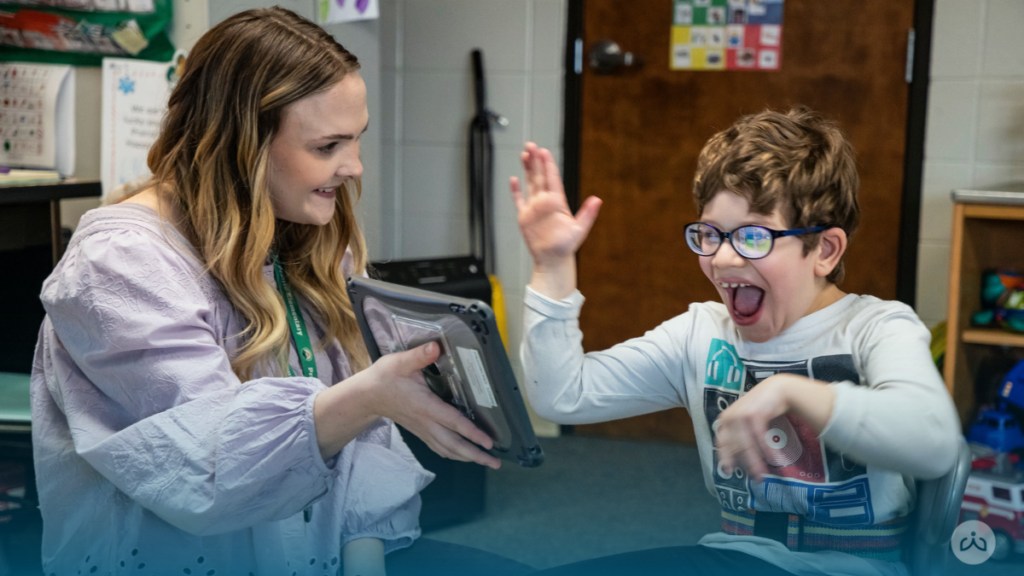 Student excitedly responds while engaging with a Readtopia literacy activity on a tablet with his teacher.
