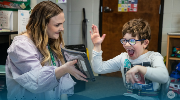 Student excitedly responds while engaging with a Readtopia literacy activity on a tablet with his teacher.