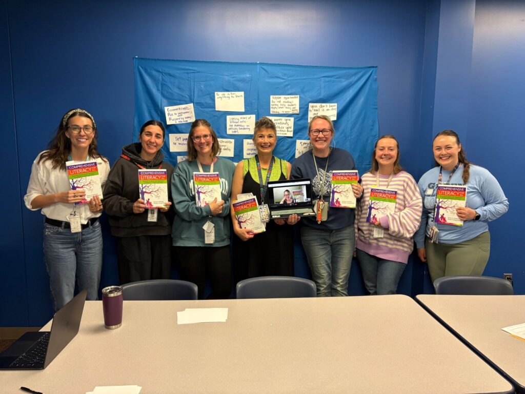 Seven early childhood educators hold copies of Comprehensive Literacy for All while a virtual participant joins the literacy book club on a laptop.